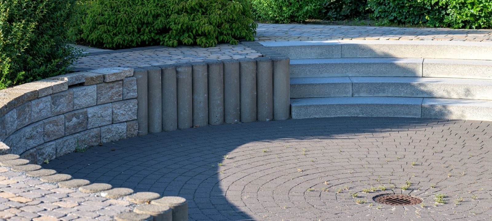 Runde Pflasterfläche mit Palisaden, Natursteinmauer und Stufen